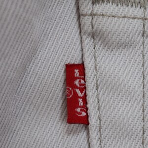 May include: A close-up of a white denim fabric with a red Levi's patch sewn onto the fabric. The patch has white stitching and the Levi's logo is visible.