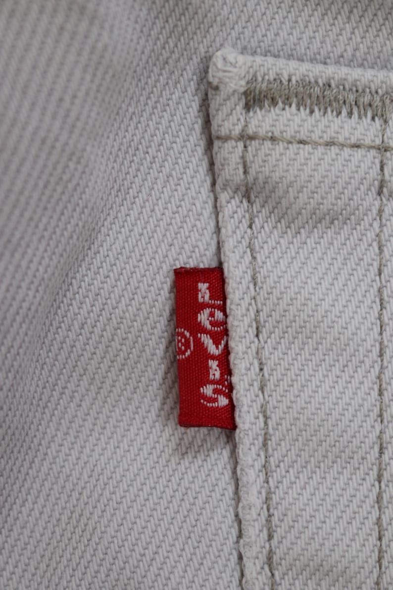 May include: A close-up of a white denim fabric with a red Levi's patch sewn onto the fabric. The patch has white stitching and the Levi's logo is visible.