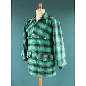 May include: A green and black plaid jacket with a collared neckline, two chest pockets, and two lower pockets. The jacket has silver-colored buttons and is displayed on a mannequin.