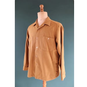 Peut inclure: Chemise à manches longues de couleur beige avec deux poches de poitrine et une fermeture boutonnée, présentée sur un mannequin. La chemise a un col et des poignets boutonnés. Le tissu semble être du velours côtelé ou une matière similaire texturée. La chemise est de couleur unie.