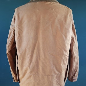 May include: A tan-colored jacket with a corduroy collar, displayed on a mannequin. The jacket has a button closure and two pockets. The background is a solid teal color.