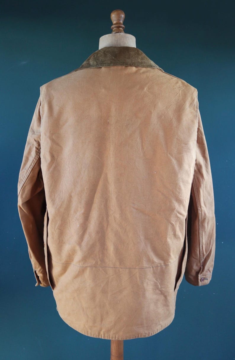 May include: A tan-colored jacket with a corduroy collar, displayed on a mannequin. The jacket has a button closure and two pockets. The background is a solid teal color.