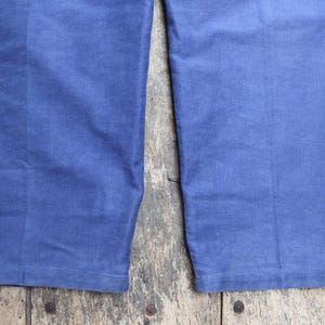 May include: Close-up of the bottom of a pair of blue denim trousers. The fabric is a dark blue and the seams are visible.