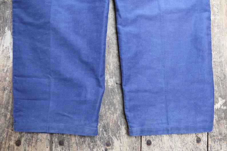 May include: Close-up of the bottom of a pair of blue denim trousers. The fabric is a dark blue and the seams are visible.
