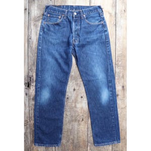 May include: Classic blue denim jeans with a button fly, five-pocket design, and a faded wash. The jeans have a straight leg cut and are displayed against a rustic wooden background. A timeless wardrobe staple.