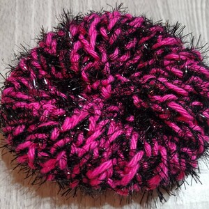 Puede incluir: Un pomp&oacute;n de lana rosa y negro peludo con un acabado brillante.