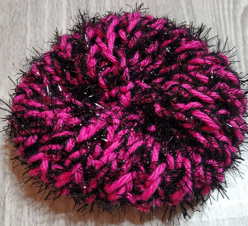 Puede incluir: Un pomp&oacute;n de lana rosa y negro peludo con un acabado brillante.
