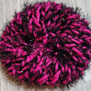 Puede incluir: Un gorro de punto rosa y negro peludo con hilos brillantes.