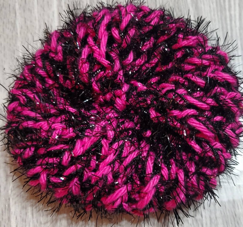 Puede incluir: Un gorro de punto rosa y negro peludo con hilos brillantes.
