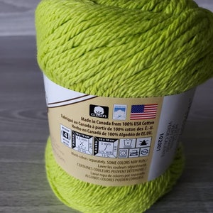 May include: A skein of bright green cotton yarn. The label reads "Made in Canada from 100% USA Cotton" and includes information about the yarn weight, needle size, and care instructions. Wash colors separately. Some colors may run.