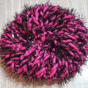 Puede incluir: Una esponja de fregar de hilo rosa y negro con un acabado brillante. La esponja est&aacute; hecha de hilo esponjoso y es perfecta para limpiar platos u otras superficies.