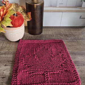 May include: A deep red knitted dishcloth with a geometric pattern. The dishcloth is made of cotton and is perfect for drying dishes or cleaning up spills.