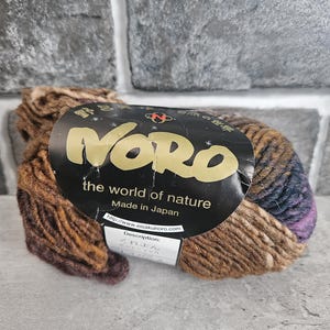 May include: A skein of Noro yarn, featuring a blend of brown, purple, and blue hues. The label reads "the world of nature" and "Made in Japan."