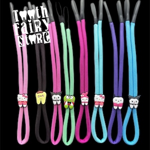 May include: Eight colorful eyeglass retainers with different cartoon character charms. The charms include a tooth, a frog, a cat, a kitty, and a tooth with a bow. The retainers are made of a stretchy cord material.