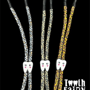 May include: Three tooth fairy necklace cords with a cute tooth charm. The cords are made of a leopard print fabric in three different color combinations: black and white, tan and black, and orange and black.