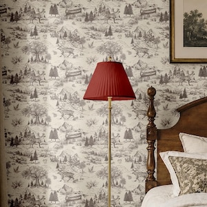 May include: A floor lamp with a slender metallic pole, a circular base, and a deep red pleated conical shade. The lamp stands against a wall covered in wallpaper featuring a repeating black and white illustration of deer, trees, and mountains.