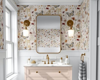 May include: A white bathroom vanity with three drawers and a lower shelf. The vanity has a white marble countertop with a gold faucet and two gold soap dispensers. The vanity is in front of a wall with white wainscoting and floral wallpaper with butterflies.