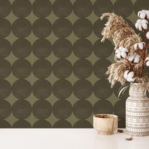Peut inclure: Papier peint vert olive avec un motif répétitif de grands cercles gris foncé. Sur une table blanche, devant le papier peint, se trouvent un vase de fleurs séchées, un bol en bois et des livres.