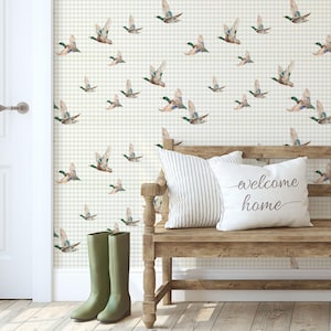 May include: A room scene with a wooden bench, pillows, and green wellington boots. The wall is decorated with a duck pattern on a light green and white checkered background. A white door is on the left. The bench has a pillow with the text "welcome home".