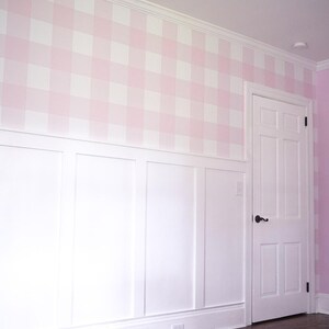 May include: A wall featuring a light pink and white gingham pattern on the upper section, with white wainscoting on the lower portion. A white six-panel door with a black handle is integrated into the wall, set against dark wood flooring.