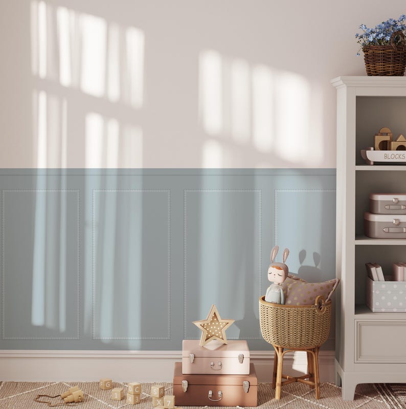 Puede incluir: Una pared azul claro con z&oacute;calo blanco y una estanter&iacute;a blanca con una estanter&iacute;a para juguetes, una estanter&iacute;a para libros y una estanter&iacute;a con una cesta de juguetes. La estanter&iacute;a est&aacute; al lado de una cesta de mimbre con un conejito de peluche y una luz nocturna en forma de estrella. Hay tres maletas apiladas delante de la cesta.