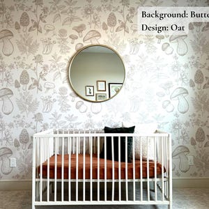 K&ouml;nnte beinhalten: Ein wei&szlig;es Babybett mit einer braunen Matratze und einem schwarzen Kissen in einem Kinderzimmer mit einer wei&szlig;en Wand, die mit einem Tapetendesign aus braunen Pilzen und Pflanzen verziert ist. Der Text "Background: Buttermilk Design: Oat" steht in der oberen rechten Ecke des Bildes.