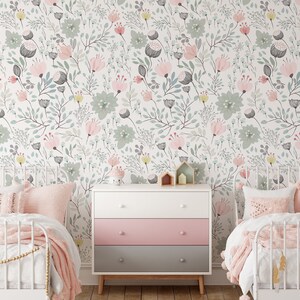 May include: Two white twin beds with pink bedding and pillows in a room with a white dresser with pink and gray drawers. The walls are covered in a floral wallpaper with pink, green, and yellow flowers.