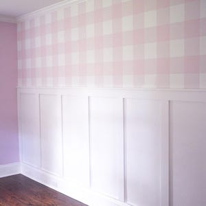 May include: A wall featuring a top section covered in light pink and white gingham patterned wallpaper and a bottom section finished with white board and batten wainscoting. The wall includes a white crown molding at the top and a white baseboard.