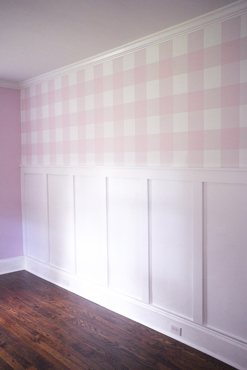 May include: A wall featuring a top section covered in light pink and white gingham patterned wallpaper and a bottom section finished with white board and batten wainscoting. The wall includes a white crown molding at the top and a white baseboard.