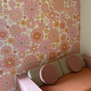 May include: A pink and orange floral patterned wallpaper with a light pink and beige couch with two pink pillows. The couch has a light pink armrest.