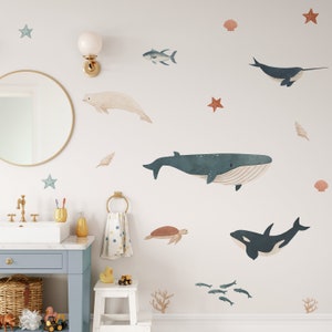 May include: A white bathroom with a blue vanity and a mirror. The wall has a variety of ocean-themed decals, including whales, fish, seashells, and starfish.