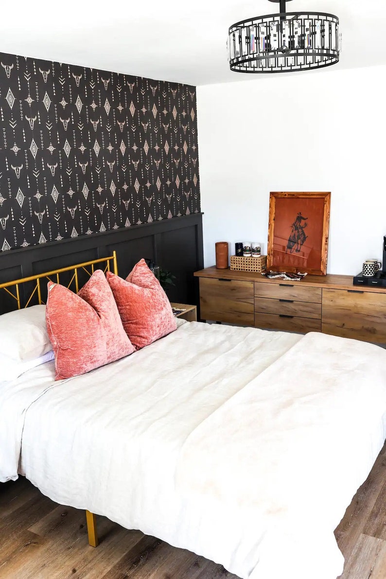 Bedroom overview with Western wallpaper, gold bed frame, white and coral bedding, wooden dresser, and a chandelier.