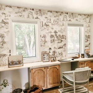 K&ouml;nnte beinhalten: Ein Heimb&uuml;ro mit einem hellen Holzschreibtisch und zwei St&uuml;hlen. Die W&auml;nde sind mit einer braunen und wei&szlig;en Tapete mit Toile-Muster bedeckt. Es gibt zwei Fenster mit wei&szlig;en Jalousien. Eine braune Ledertasche liegt auf dem Boden neben einer Topfpflanze.