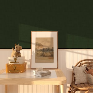 May include: A wooden table with a framed landscape painting, a stack of books, and a small stuffed dog on top of two vintage suitcases. The table is in front of a green wall with white wainscoting.