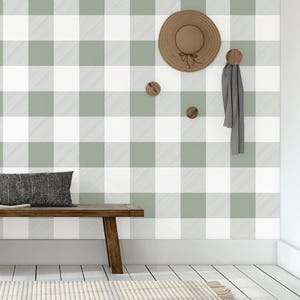 Op de afbeelding: Een houten bank met een grijs en wit buffalo plaid behang erachter. Er hangt een strohoed aan een haak aan de muur, samen met een grijze sjaal.