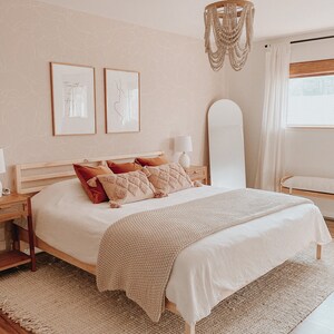 May include: A white bed with a beige knitted throw blanket and a wooden frame. The bed has a white headboard and a beige rug underneath. There are two framed prints on the wall behind the bed, one with the text "Together is our favorite place to be" and the other with a line drawing of a couple. There is a white beaded chandelier hanging from the ceiling above the bed.