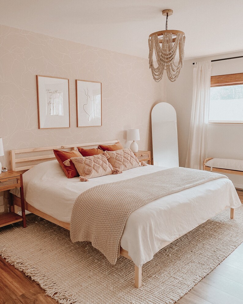 May include: A white bed with a beige knitted throw blanket and a wooden frame. The bed has a white headboard and a beige rug underneath. There are two framed prints on the wall behind the bed, one with the text "Together is our favorite place to be" and the other with a line drawing of a couple. There is a white beaded chandelier hanging from the ceiling above the bed.