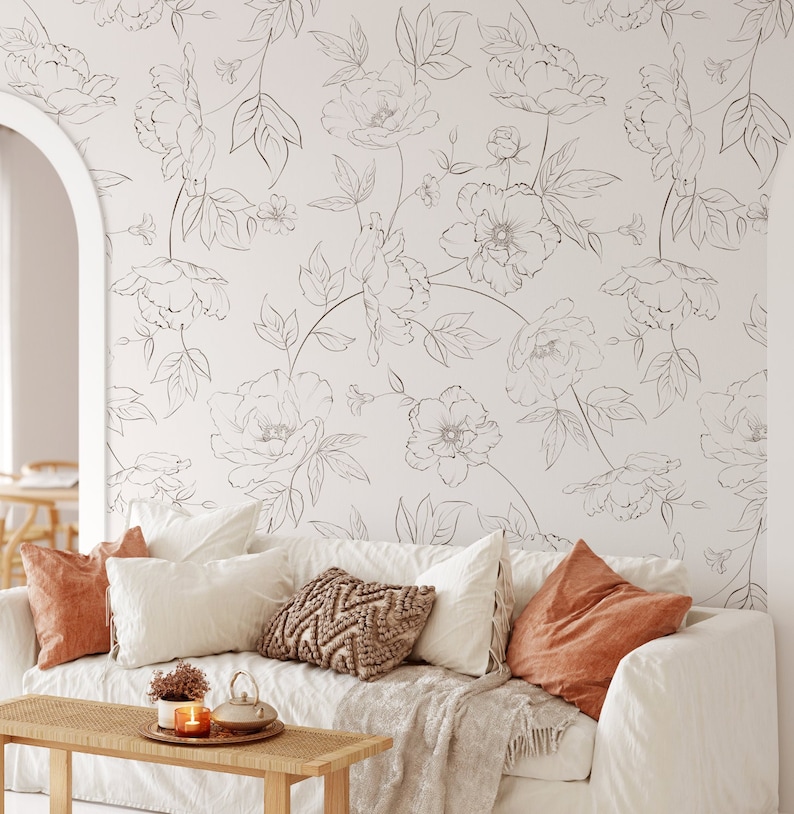 May include: A white couch with a floral patterned wall behind it. The couch has a white throw blanket, a brown throw pillow, and two orange throw pillows.