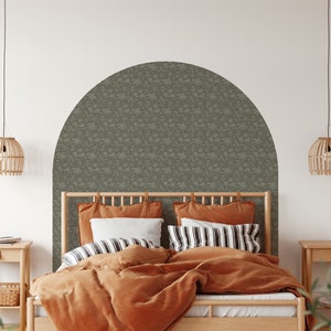 Op de afbeelding: Een slaapkamer met een houten bedframe en een hoofdeinde met een groene, gepatroneerde behang. Het bed is opgemaakt met oranje en witte beddengoed en kussens. Er zijn twee nachtkastjes met lampen en een plant in de hoek.