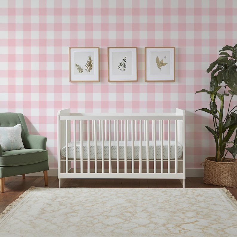 May include: A white wooden crib with vertical slats and a mattress featuring a subtle pattern, positioned against a wall with pink and white gingham wallpaper, flanked by a green armchair and a tall green plant in a woven basket.