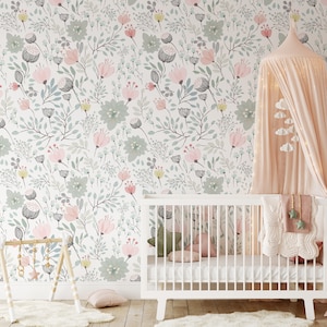May include: A white crib with a pink and green floral wallpaper in the background. The crib has a white mattress and a white blanket with a pink and white pattern. There is a pink canopy over the crib.