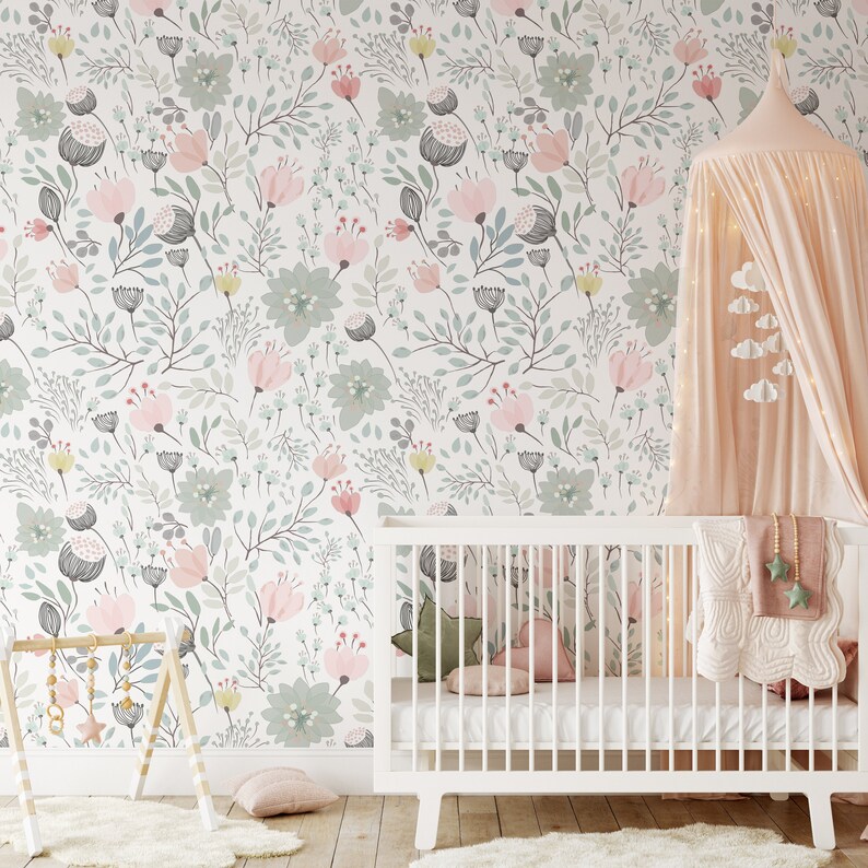 May include: A white crib with a pink and green floral wallpaper in the background. The crib has a white mattress and a white blanket with a pink and white pattern. There is a pink canopy over the crib.