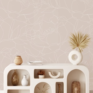 May include: A white shelf unit with arched openings, featuring various home decor items, including vases, bowls, plants, and a lamp. The shelf unit is set against a wall with a light pink background and a white abstract floral pattern.