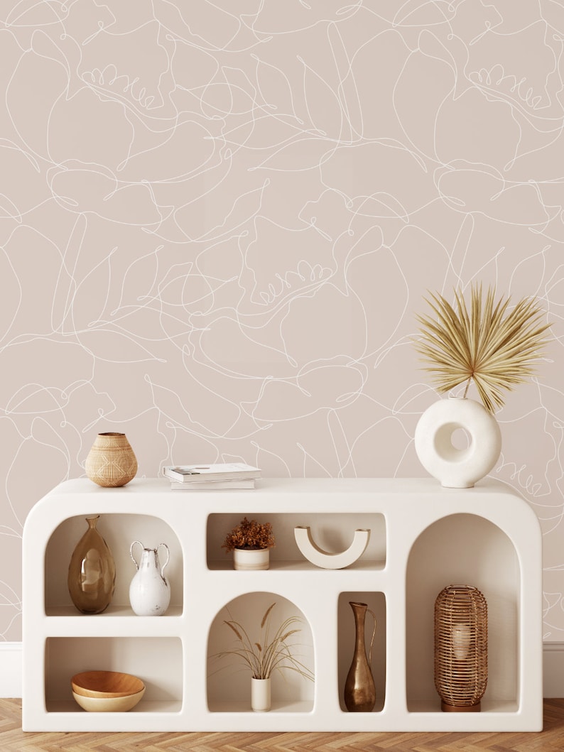 May include: A white shelf unit with arched openings, featuring various home decor items, including vases, bowls, plants, and a lamp. The shelf unit is set against a wall with a light pink background and a white abstract floral pattern.