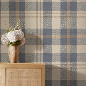 May include: Blue, beige, and tan plaid wallpaper. The pattern features a classic tartan design with intersecting lines creating a grid-like appearance. A wooden cabinet with a woven front and a vase of white flowers sits in front of the wallpaper.