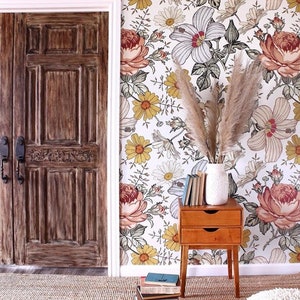 Puede incluir: Un papel tapiz floral con fondo blanco y grandes flores rosas, amarillas y blancas. Una puerta de madera est&aacute; en el lado izquierdo de la imagen, y una peque&ntilde;a mesita de noche de madera con dos cajones est&aacute; en el lado derecho de la imagen. La mesita de noche tiene un jarr&oacute;n blanco con hierba de la pampa seca en la parte superior. Una pila de libros est&aacute; en el suelo frente a la mesita de noche.