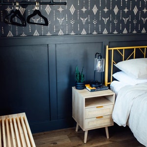 Bedroom detail with Western wallpaper, blue panel wall, wood bedside table with a lantern lamp, and plant.