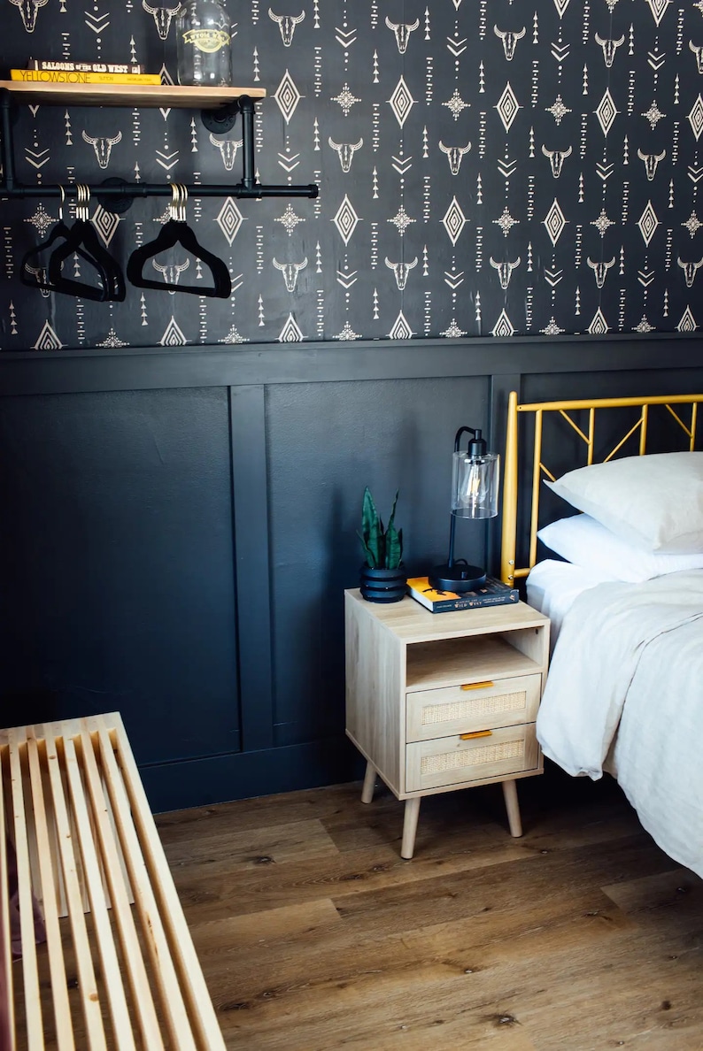 Bedroom detail with Western wallpaper, blue panel wall, wood bedside table with a lantern lamp, and plant.