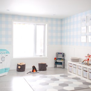 May include: A playroom with a blue and white gingham wallpaper, a white play kitchen, a camper tent, and a gray and white rug.