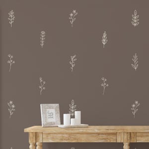 Puede incluir: Una pared marrón con dibujos lineales florales blancos. Una mesa de madera exhibe una foto enmarcada con las palabras "home sweet home", velas blancas y una hoja decorativa. El tema es la decoración del hogar.